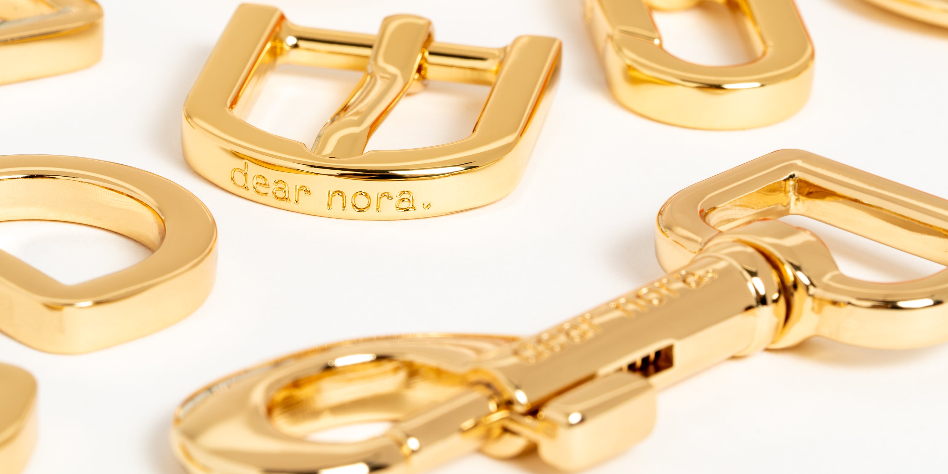 Macro shot close up of 24k gold plated metal hardware with Dear Nora engraved on the buckle and dog hook